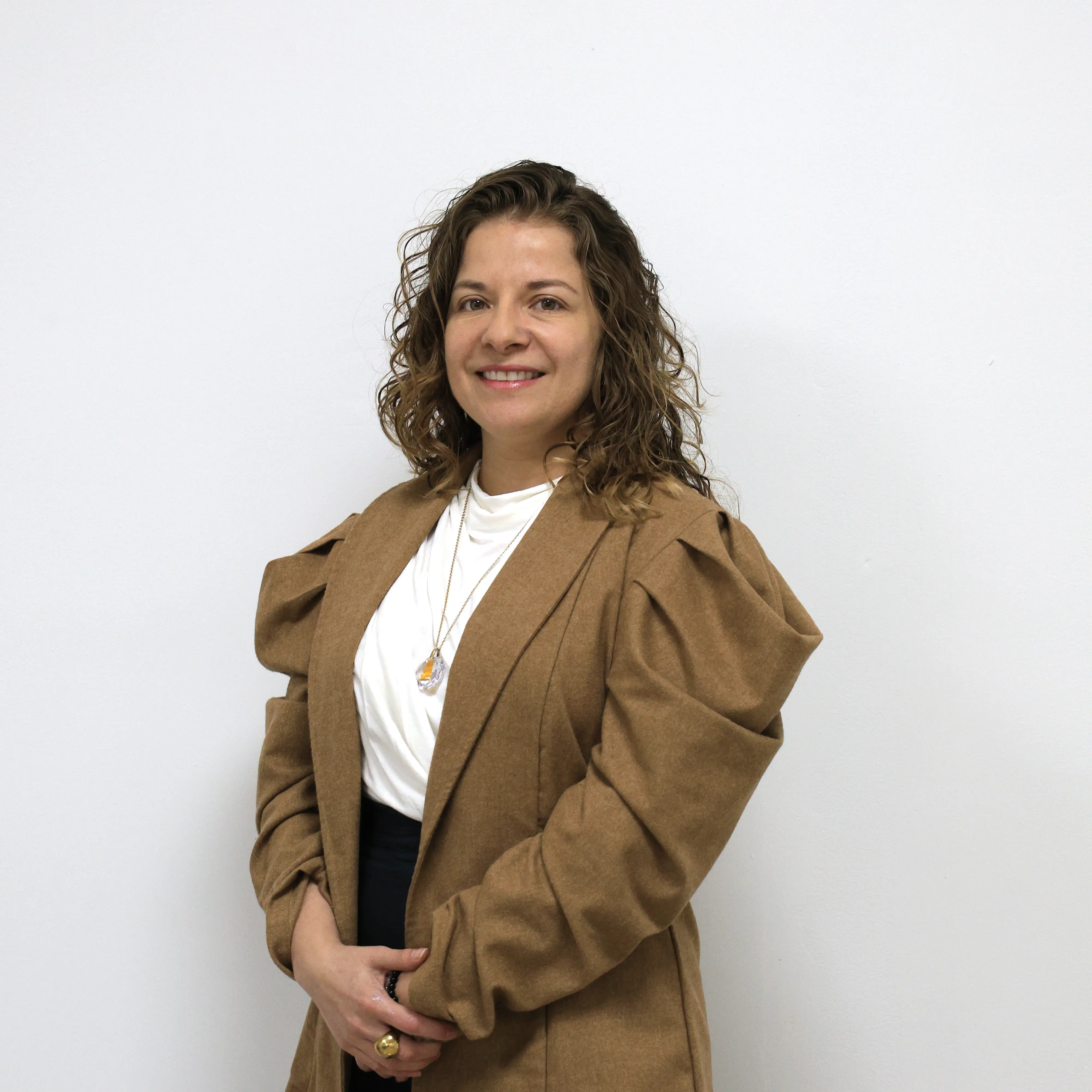 Mujer joven y sonriente, con cabello castaño claro. Vestida con blusa blanca y abrigo café