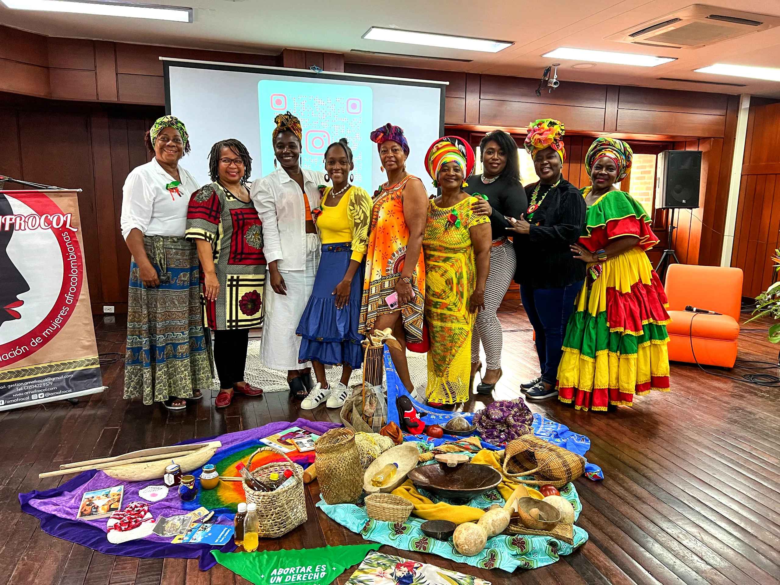 Grupo de mujeres afro, negras,raizales y palenqueras posan alegres frente a la cámara detrás de una serie de productos artesanales y tejidos representativos de sus regiones