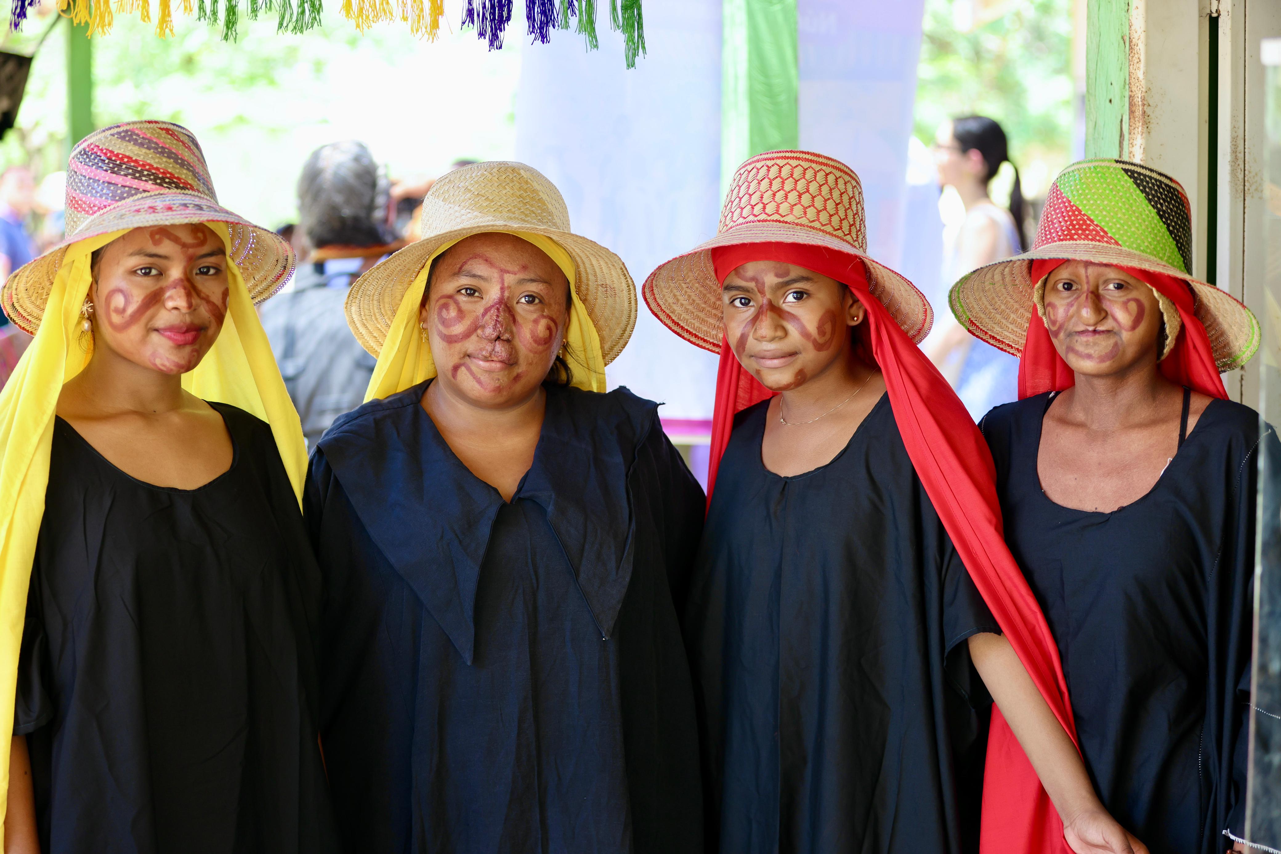 Cuatro mujeres Wayúu de La Guajira de pie, vestidas con sus mantas y sus rostros pintados miran sonrientes de frente a la cámara