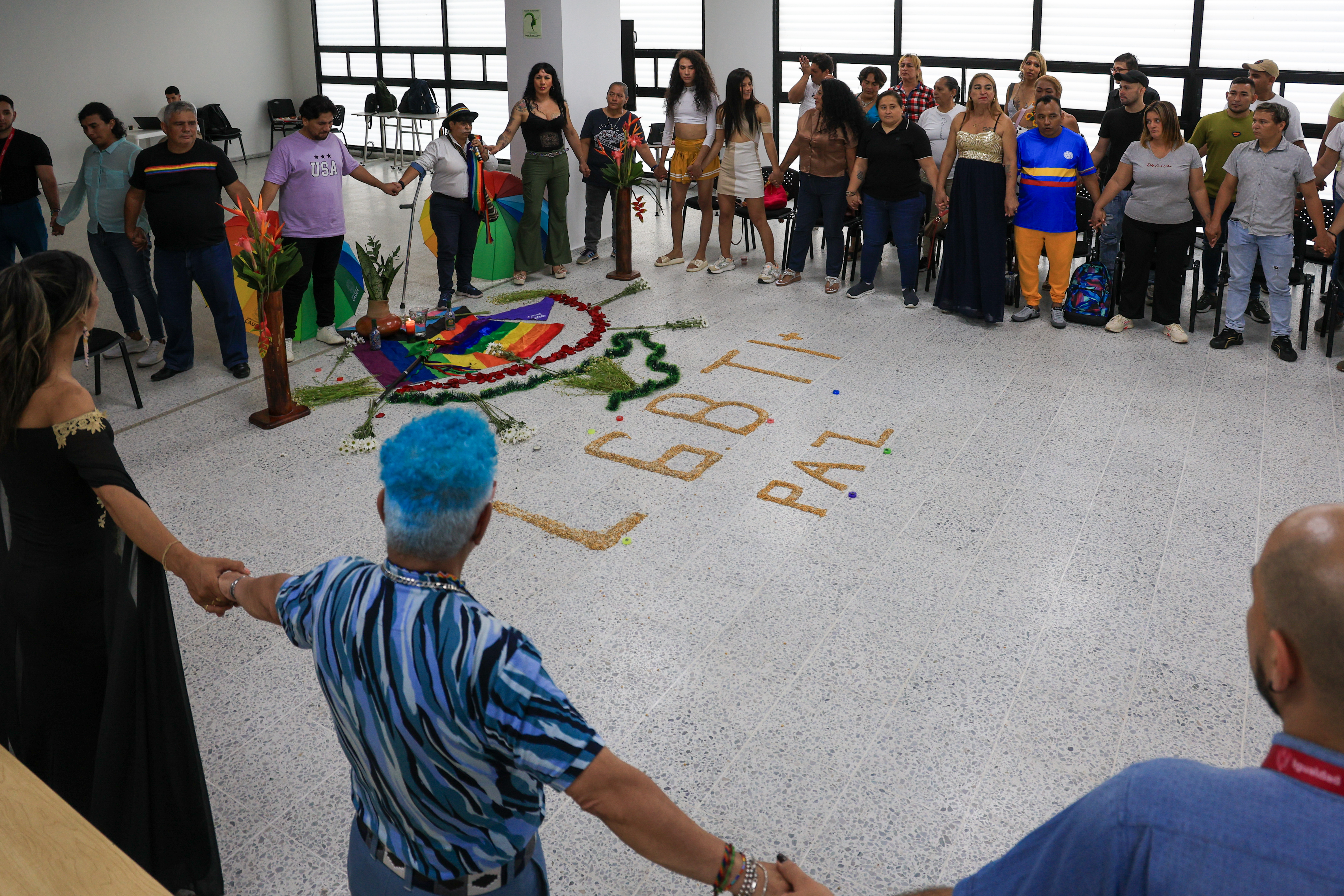 Personas de la población LGBTIQ+ tomadas de la mano  se reunen en medio de una actividad de armonización