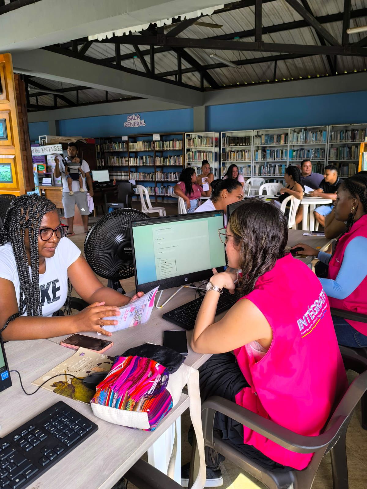Mujeres del Centro Intégrate con chalecos Magenta, atienden en la biblioteca de um colegio de Juradó a personas migrantes