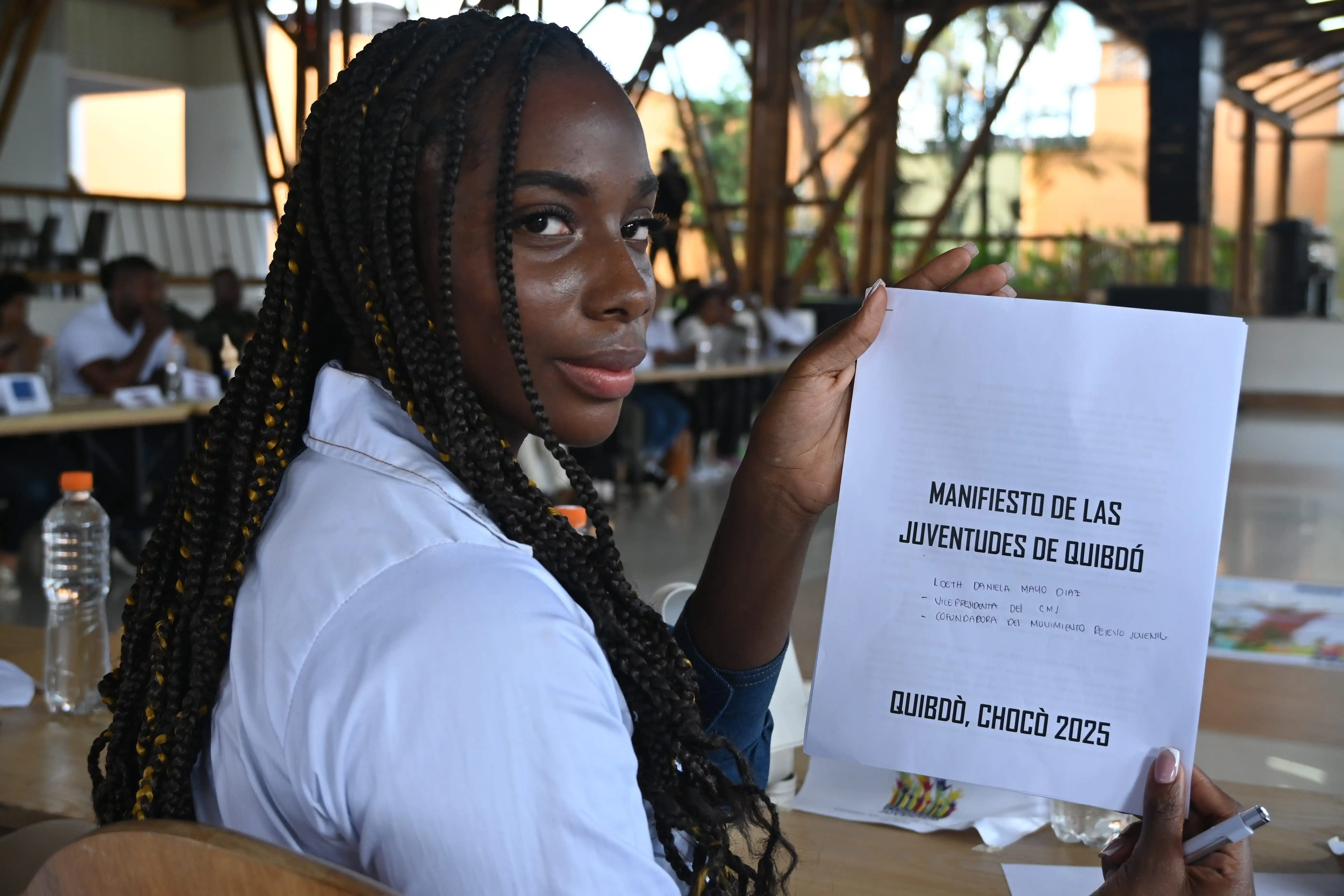 Joven mujer afro estudiante sentada en salon de reunión sostiene en su mano la carátula del documento Manifiesto de las juventudes de Quibdó 