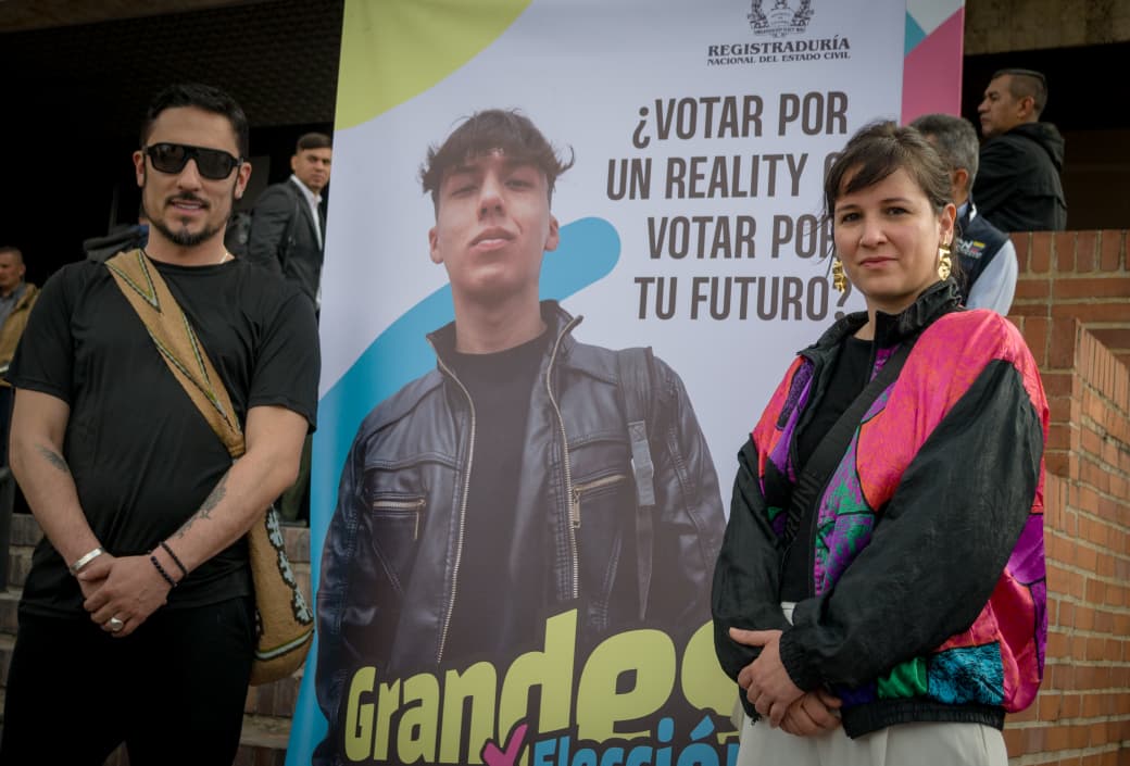 El ministro Juan Carlos Florián de pie junto a un pend{n que dice Grandea oor elección. Le acompaña en la foto la viceministra de laa Mujeres, Támara Ospina 