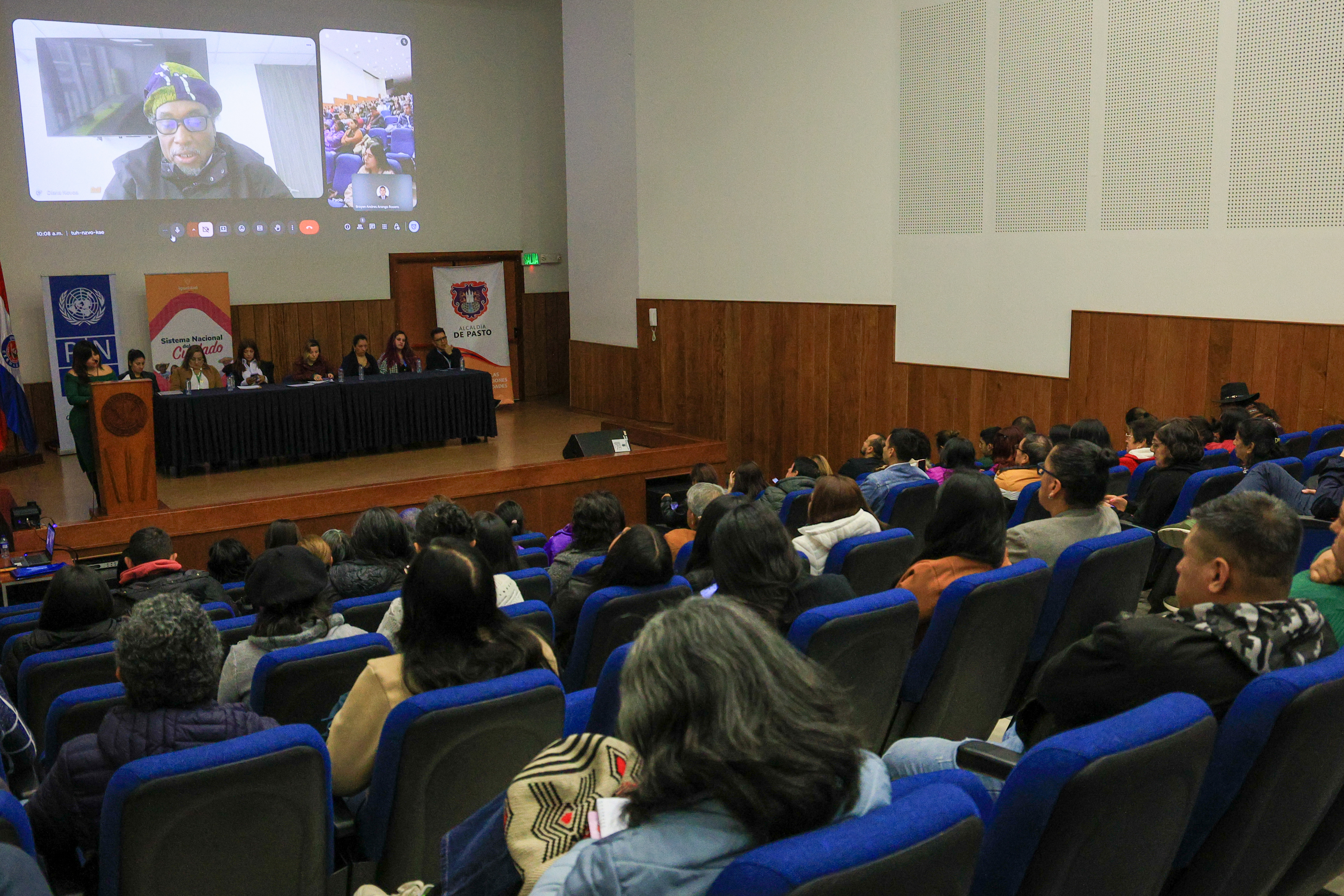 Personas sentadas en auditorio escuchan intervención del ministro Rosero Proyectada en la tarima del esceario en Pasto, Nariño