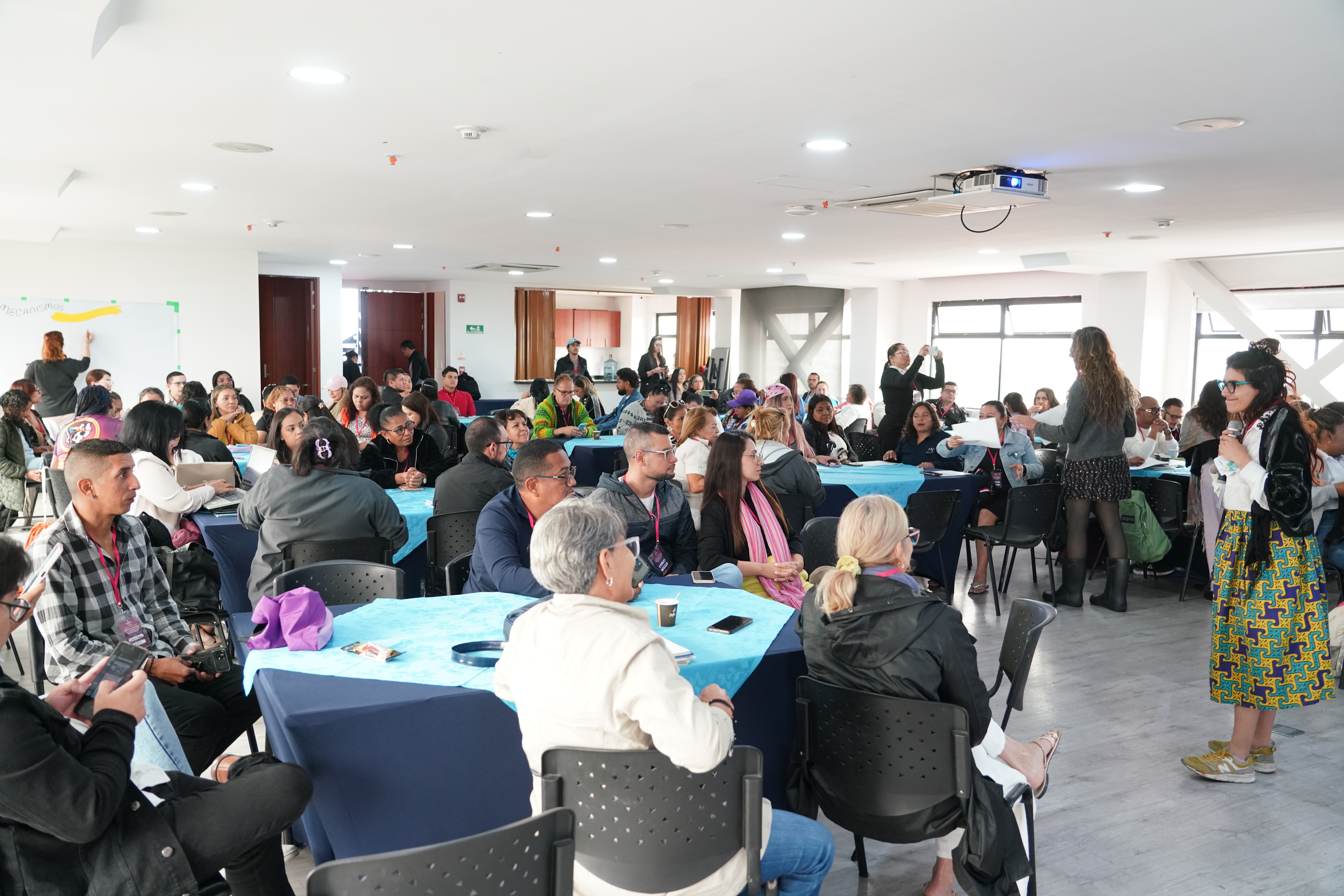 Imagen general de un salón donde se aprecia un centenar de personas que asiste a uno de los talleres del Encuentro Nacional de Migrantes 2026 que se realiza en Bogotá