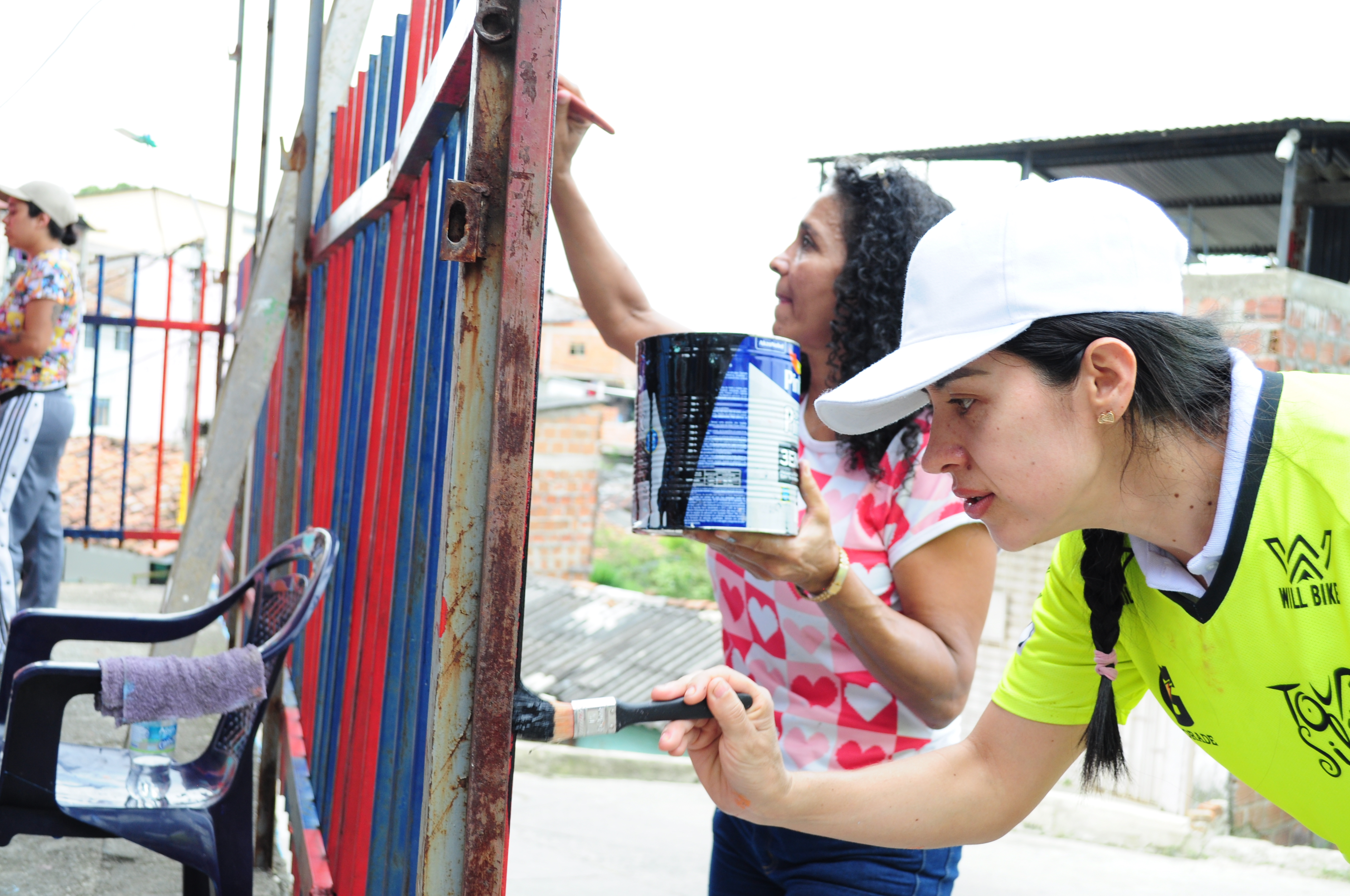 Primer plano de dos mujeres pintando la reja de una de las viviendas en el sector de Siloé.