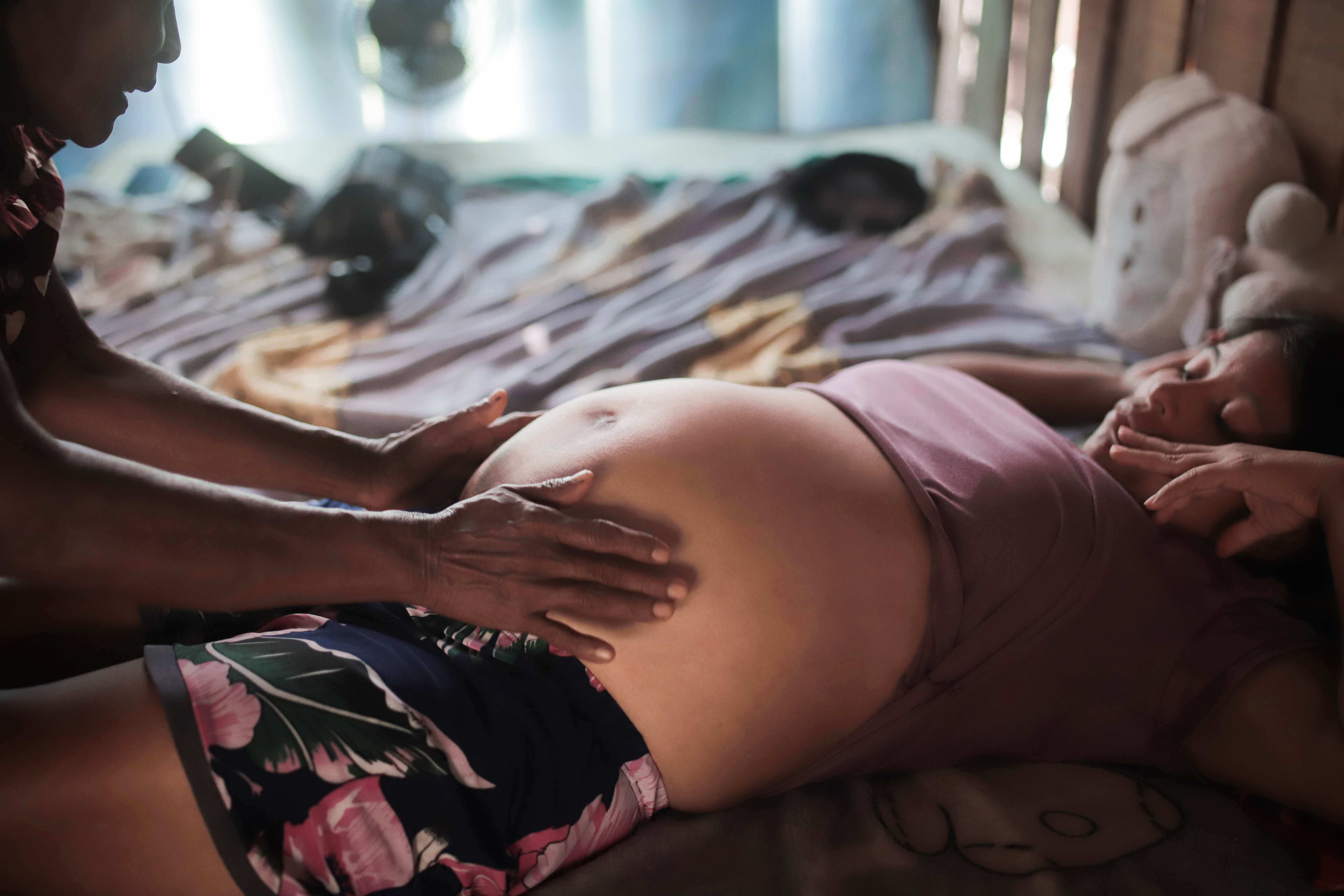 Pano medio donde de aprecia mujer afro embarazada tendoda en una cama mietras una partera con sus manos palpa el vientre de la mujer
