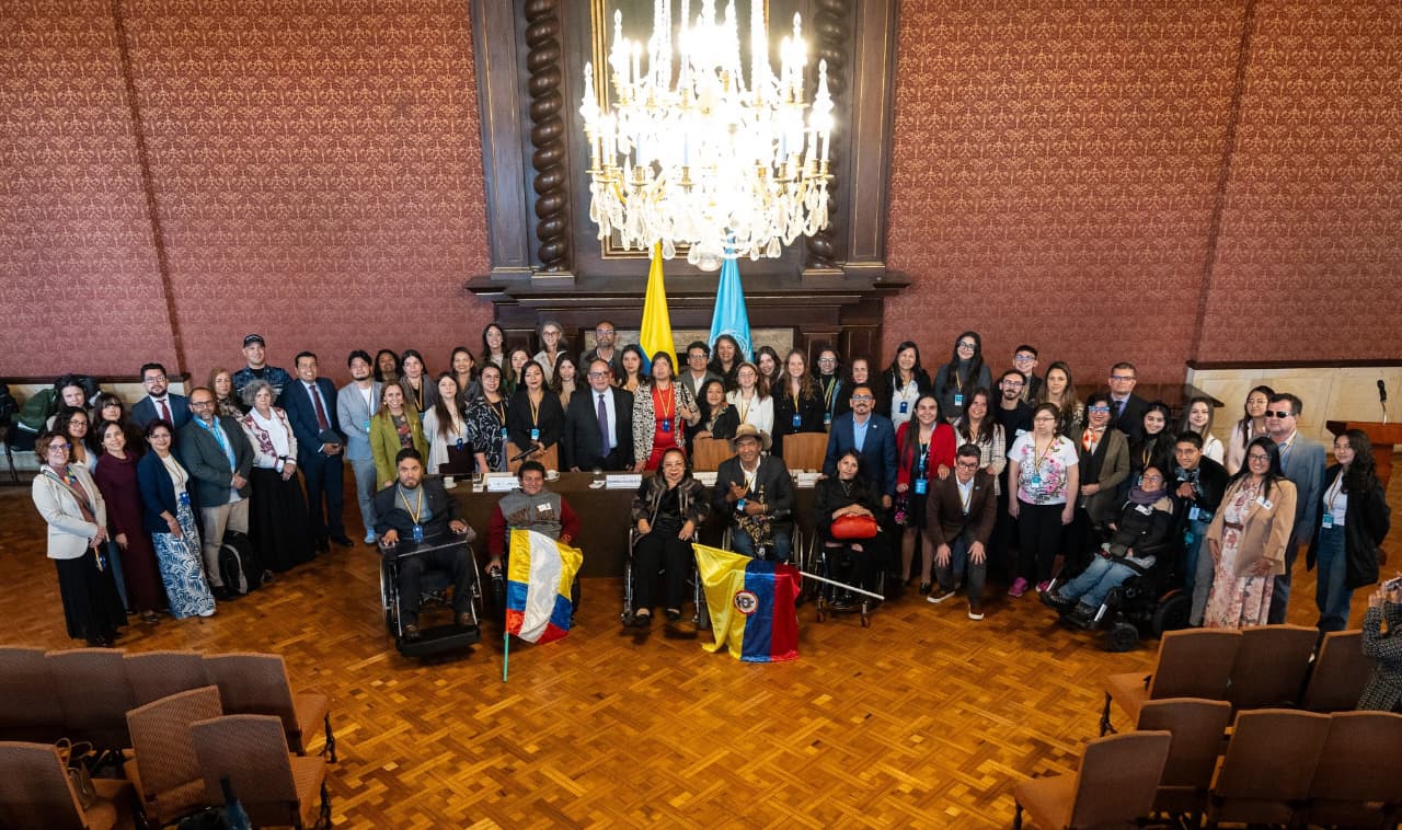 Panorámica de salón de la cancillería en Bogotá donde aparecen funcionarios de MinIgualldad y personas con discapacidad en compañía de la Relatora Especial de la ONU, Al fonde en el centro, las banderas de Colombia y la ONU