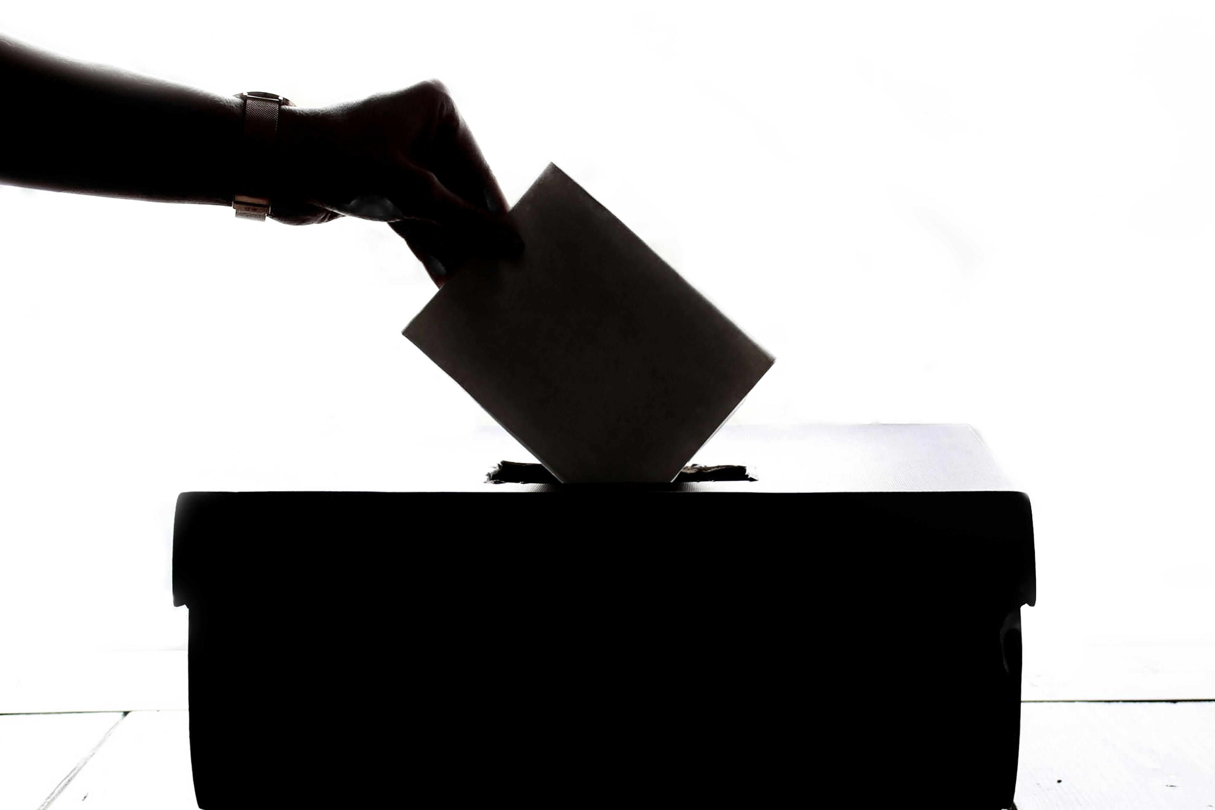 Imagen silueteada de mano depositando un voto en una urna
