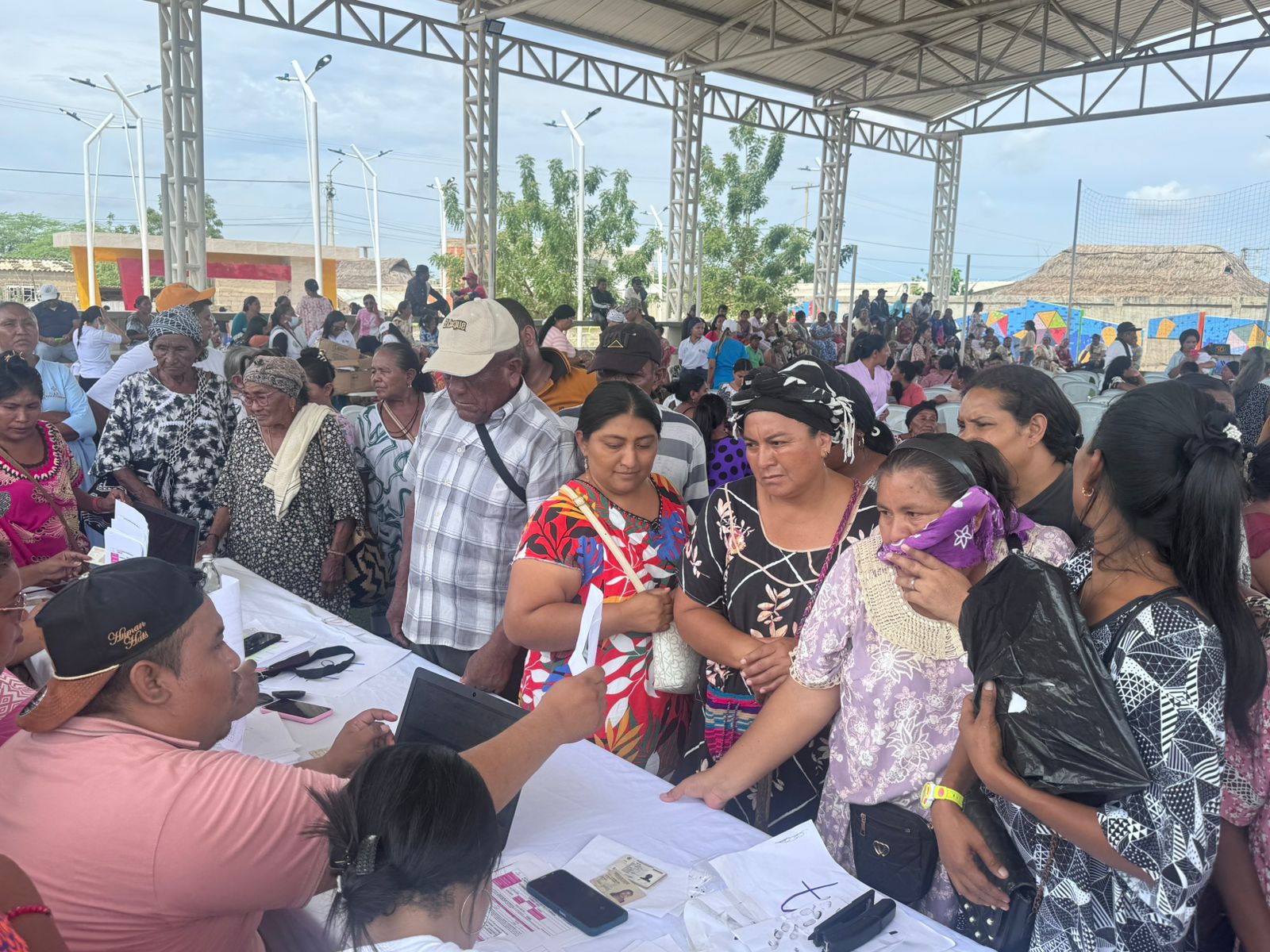 Plano general de habitantes de Riohacha bajo ujna carpa haciendo fila frente a funcionarios que están en una mesa haciendo el registro para la entrega de los alimentos