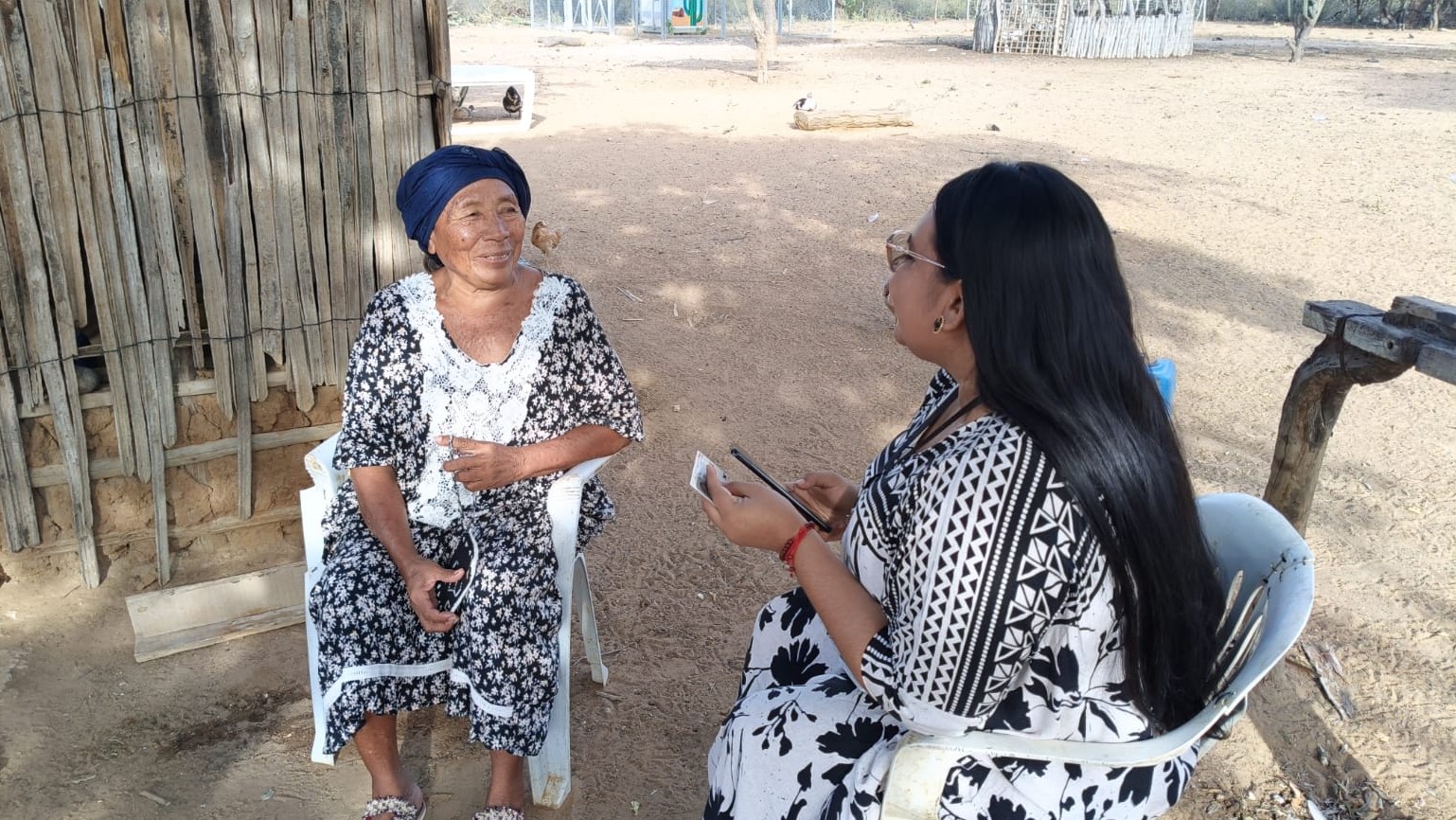 MUjer indígena de la Guajra sentada en una silla afuera de su casa atiende la visita de una de las técnicas de la Fundación Panamericana para el Desarrollo